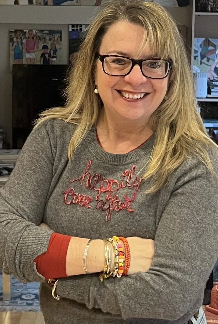 Blonde smiling woman with glasses wearing a sweater that says 'happily ever after'