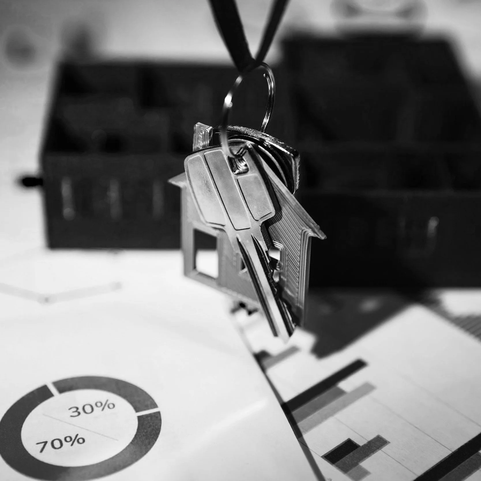 A set of keys hanging on a black lanyard, with a blurred background of a desk with charts and graphs.