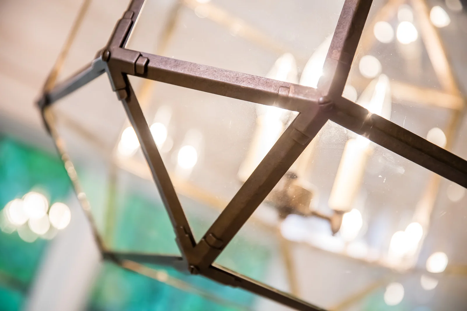 Close-up of a modern decorative hanging light fixture with a geometric metal frame and glass panels, illuminated from within.