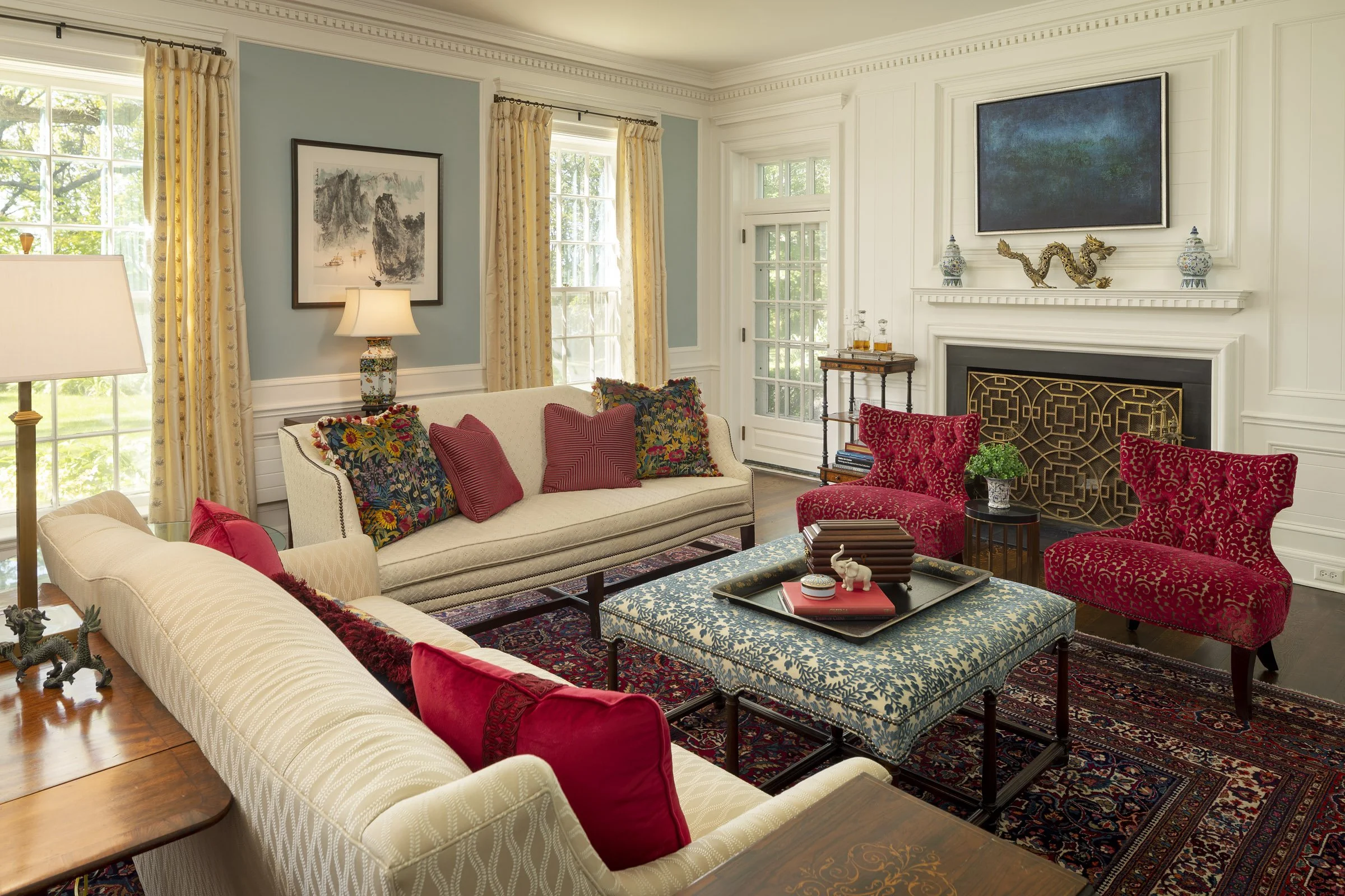 Living room with cream and red upholstered sofas, patterned accent chairs, a fireplace, decorated with art, lamps, and assorted pillows and accessories.