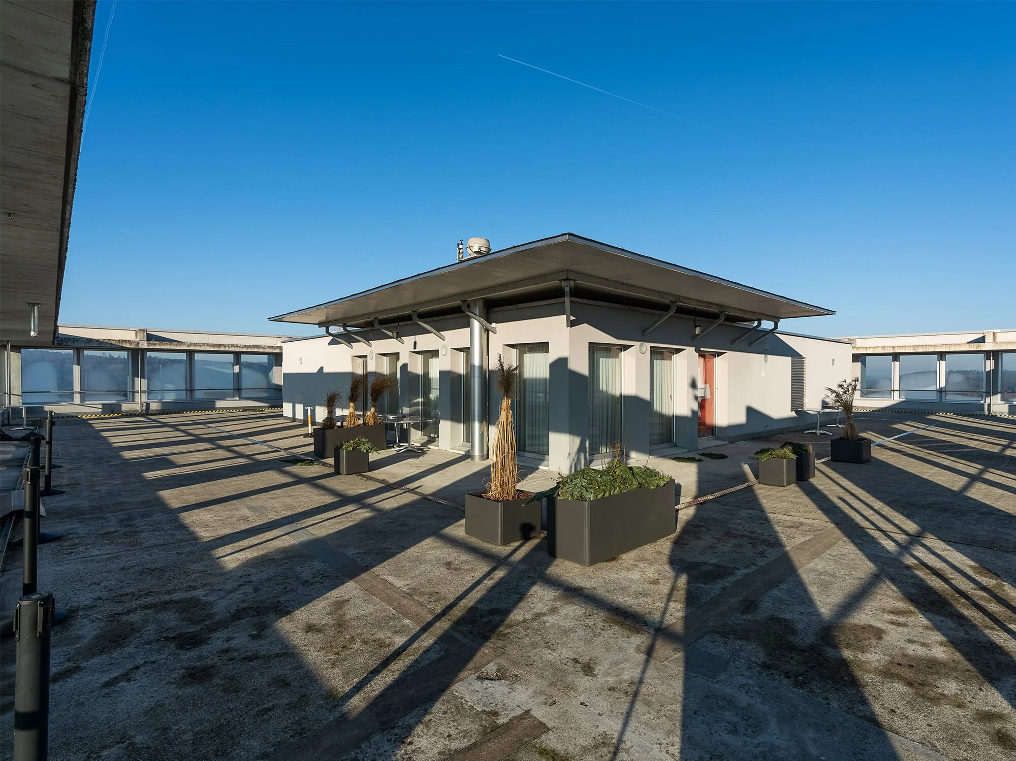 Dachterrasse mit Lounge-Möbeln, Pflanzen in Pflanzkübeln und Blick auf den blauen Himmel an einem sonnigen Tag.