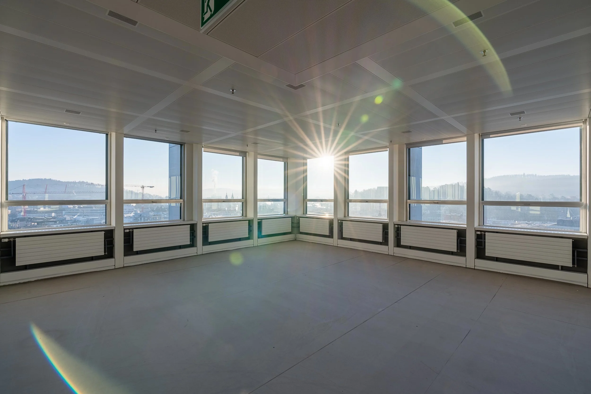 Leeres modernes Büro mit großen Fenstern und Blick auf die Stadt, Sonnenlicht strahlt in den Raum.
