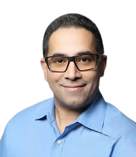 A man with glasses, dressed in a blue shirt, smiling against a black and gray background.