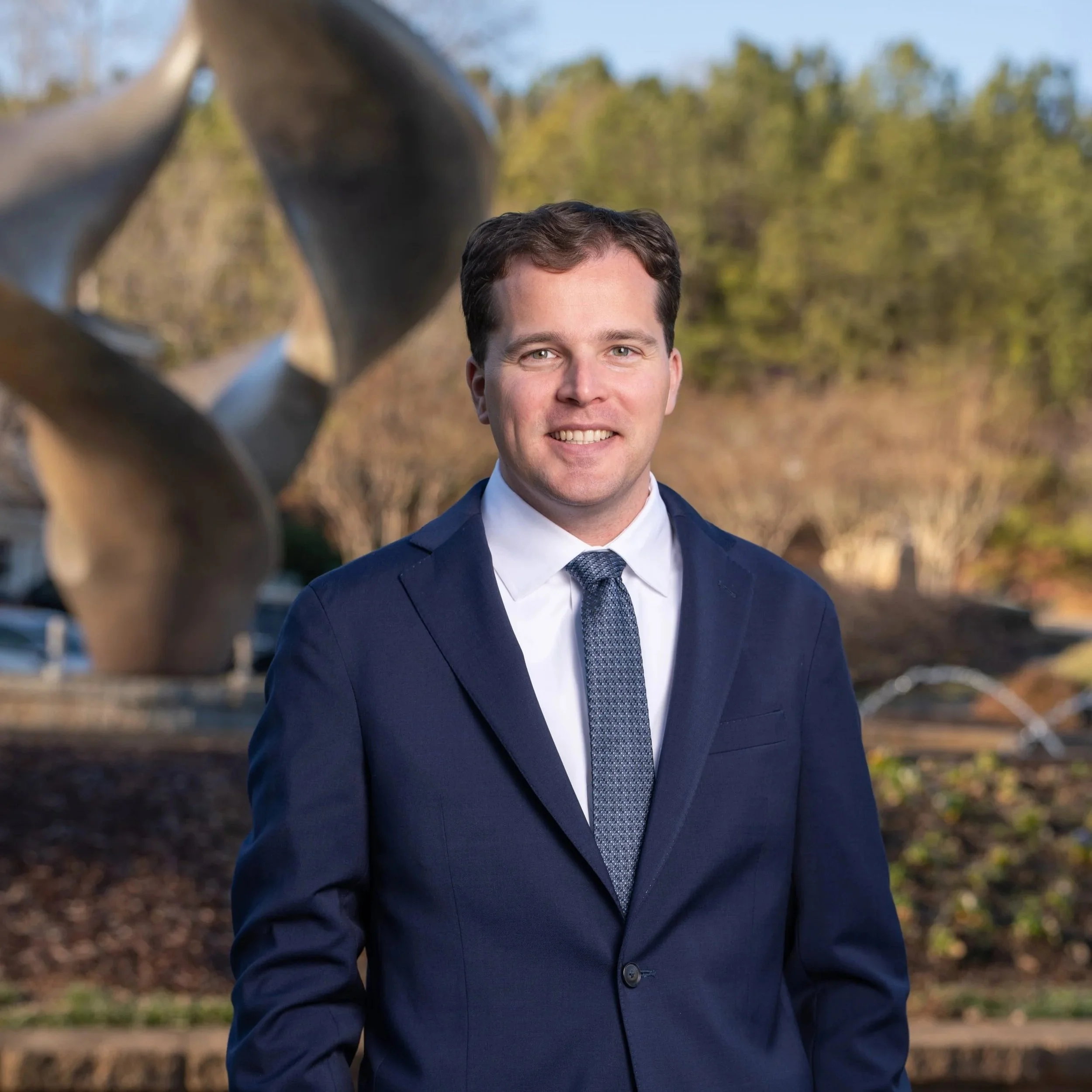 Portrait of a smiling man in a suit and white shirt against a plain white background.