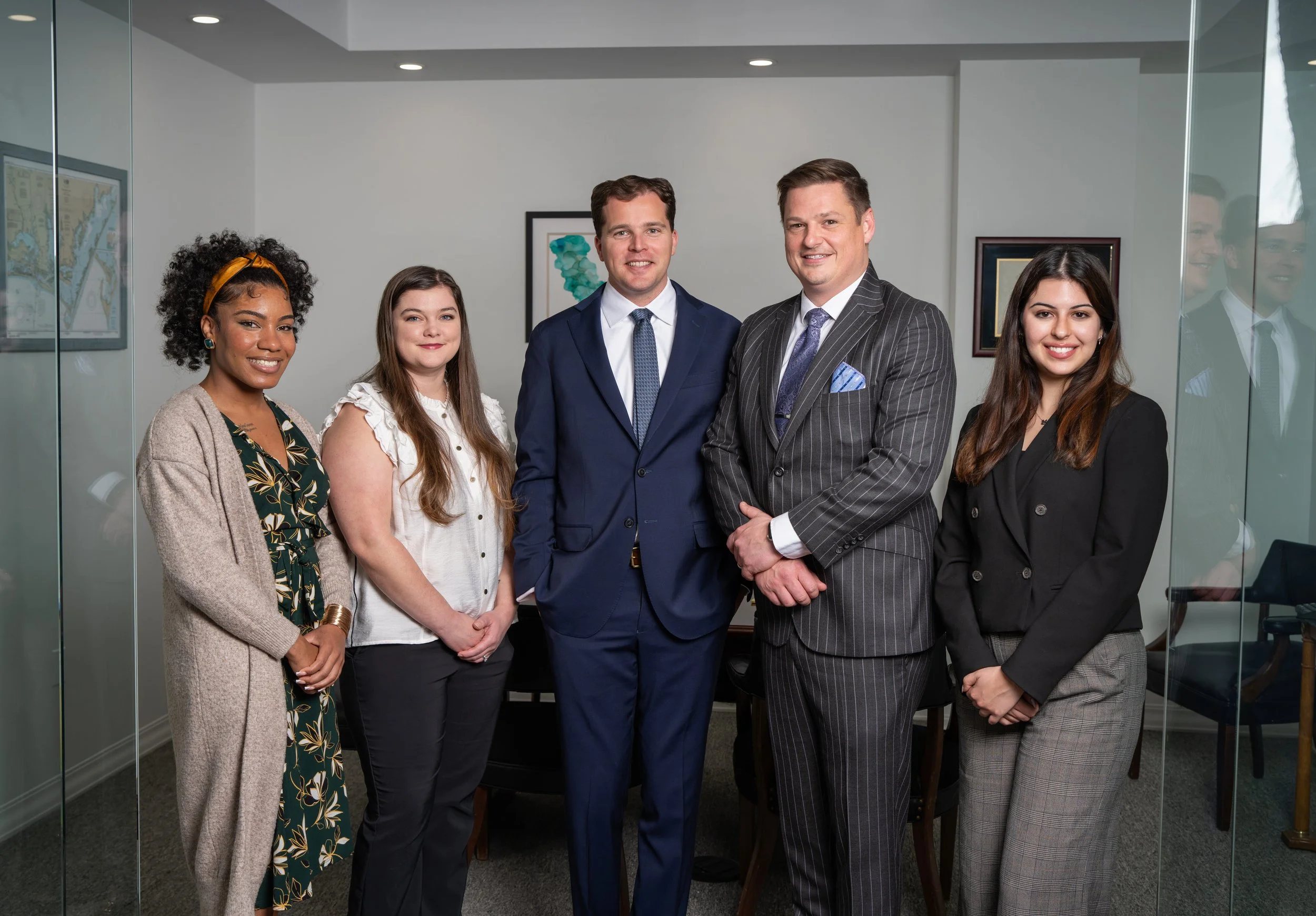 Group of five professionally dressed people standing in an office conference room, smiling at the camera.
