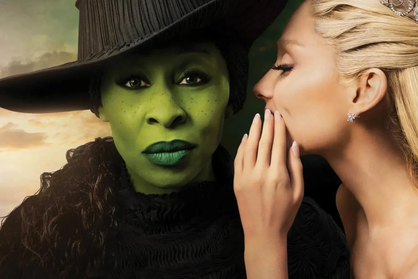 A fantasy scene featuring a woman with green, elf-like skin and freckles, wearing a large black hat and black clothing, looking directly at the camera. Beside her, a blonde woman with fair skin, closed eyes, and wearing a diamond earring, gently touches her lips with her fingers, leaning in towards her.