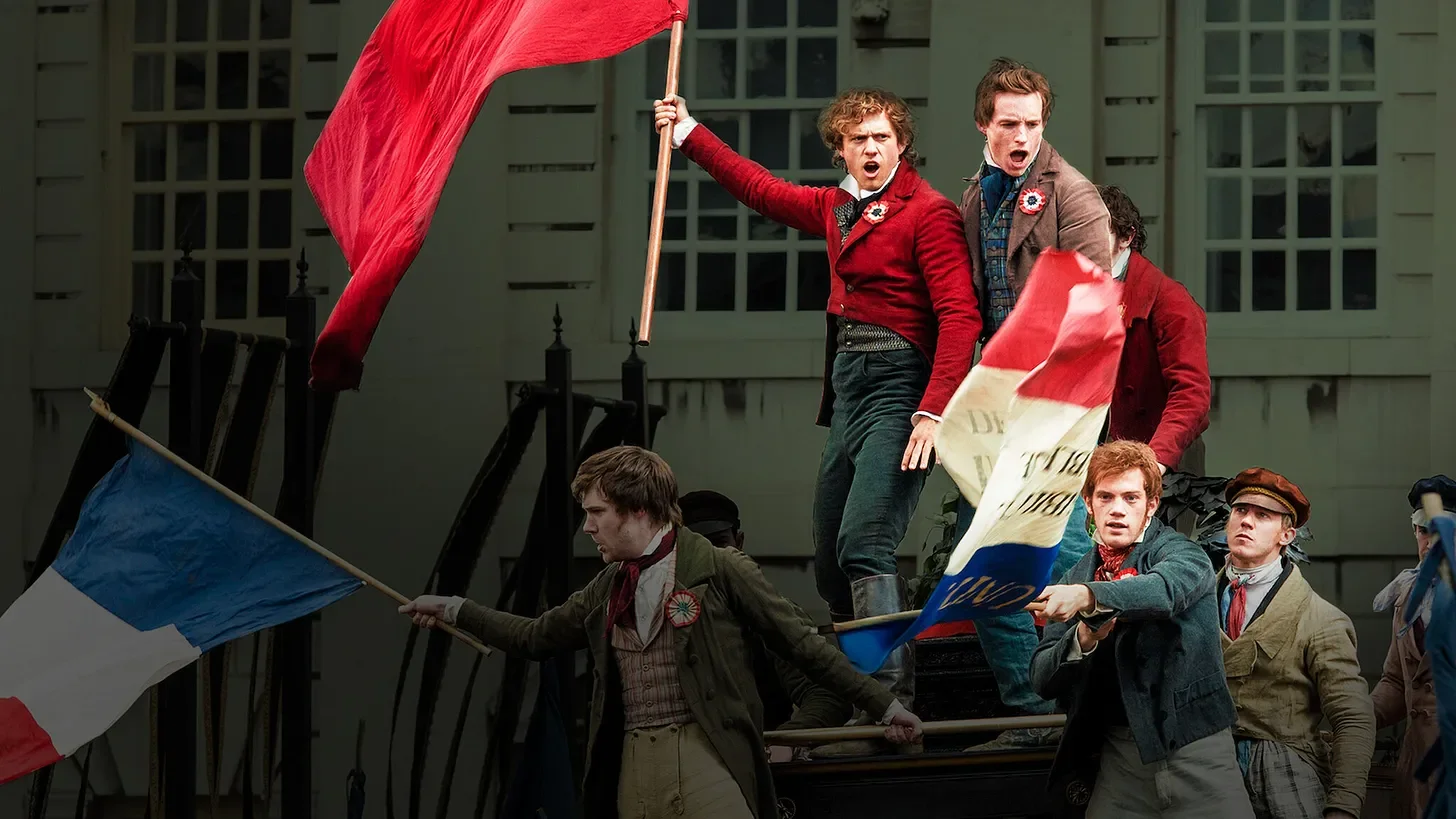 Scene from a protest or rebellion with people holding and waving French flags, some standing on a vehicle, with determined expressions.