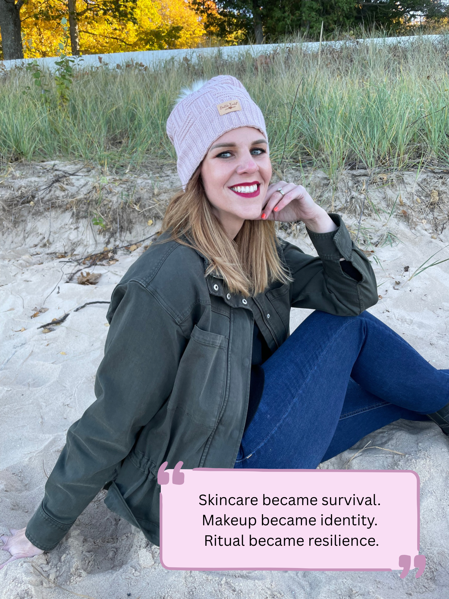 A woman with blonde hair, wearing a beige knit beanie, dark lipstick, and makeup, smiling while sitting on sand at the beach. She is dressed in a dark green jacket and blue jeans, with a background of grass, sand, and trees. There is a quote box at the bottom that says, "Skincare became survival. Makeup became identity. Ritual became resilience."