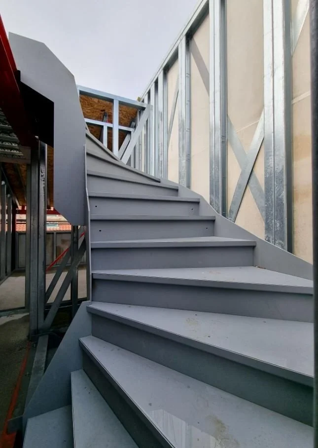 Photo of an outdoor metal staircase under construction, showing metal framing and steps with no railing.