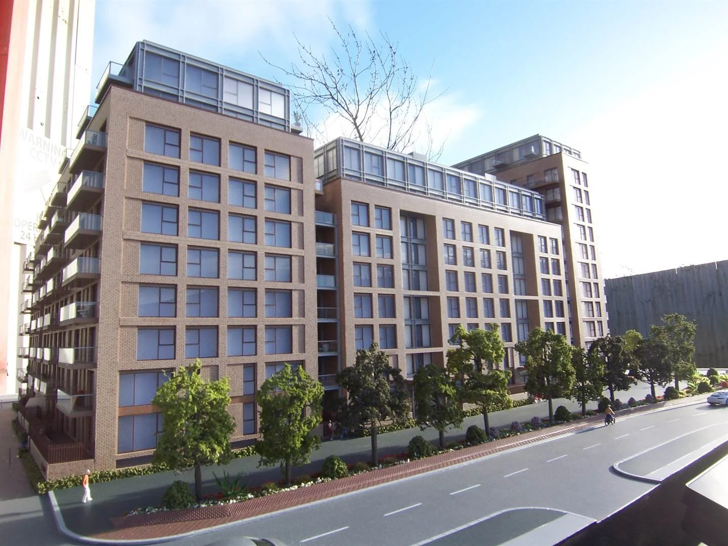 Modern multi-story residential building with brick exterior, large windows, and balconies, located along a street with trees and a sidewalk.