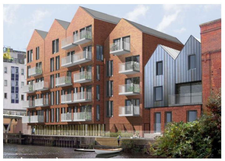 Modern apartment building with brick facade and metal panels, balconies overlooking a waterway, surrounded by greenery.