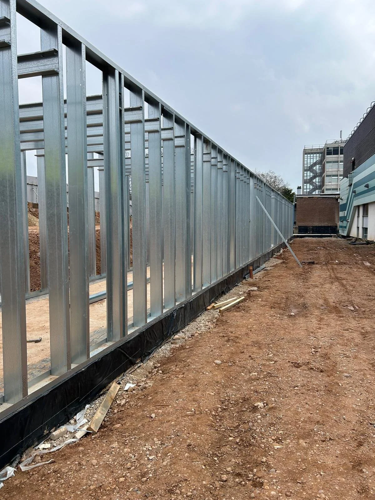 Construction site with metal framing for a building, dirt ground, and some construction materials on the ground.