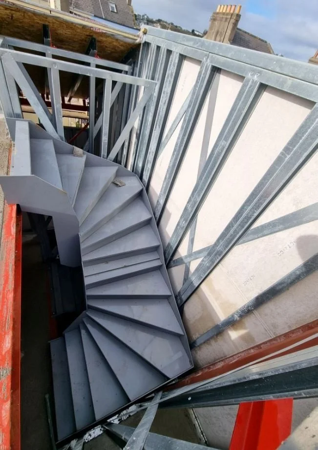 Steel spiral staircase under construction on a building site.