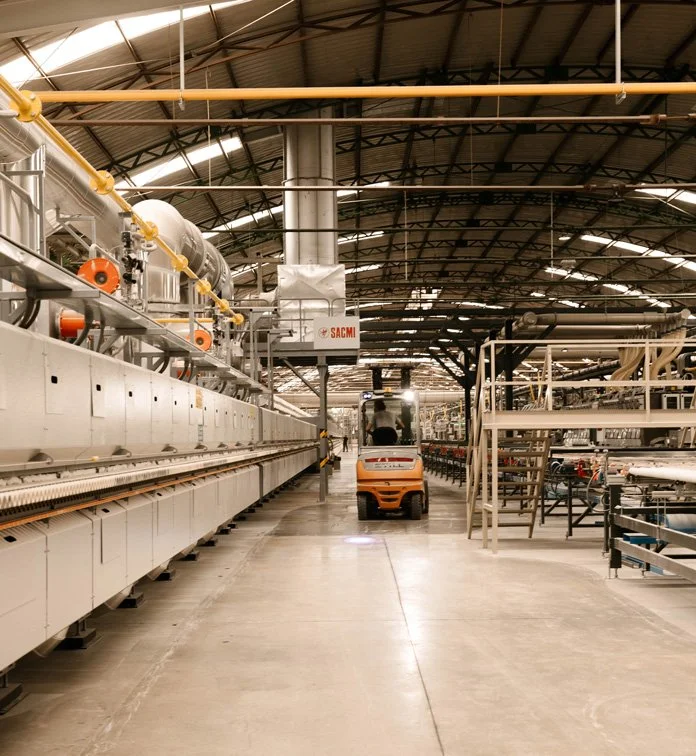 Industrial factory interior with machinery, a forklift in the center, and metal shelves on the right.