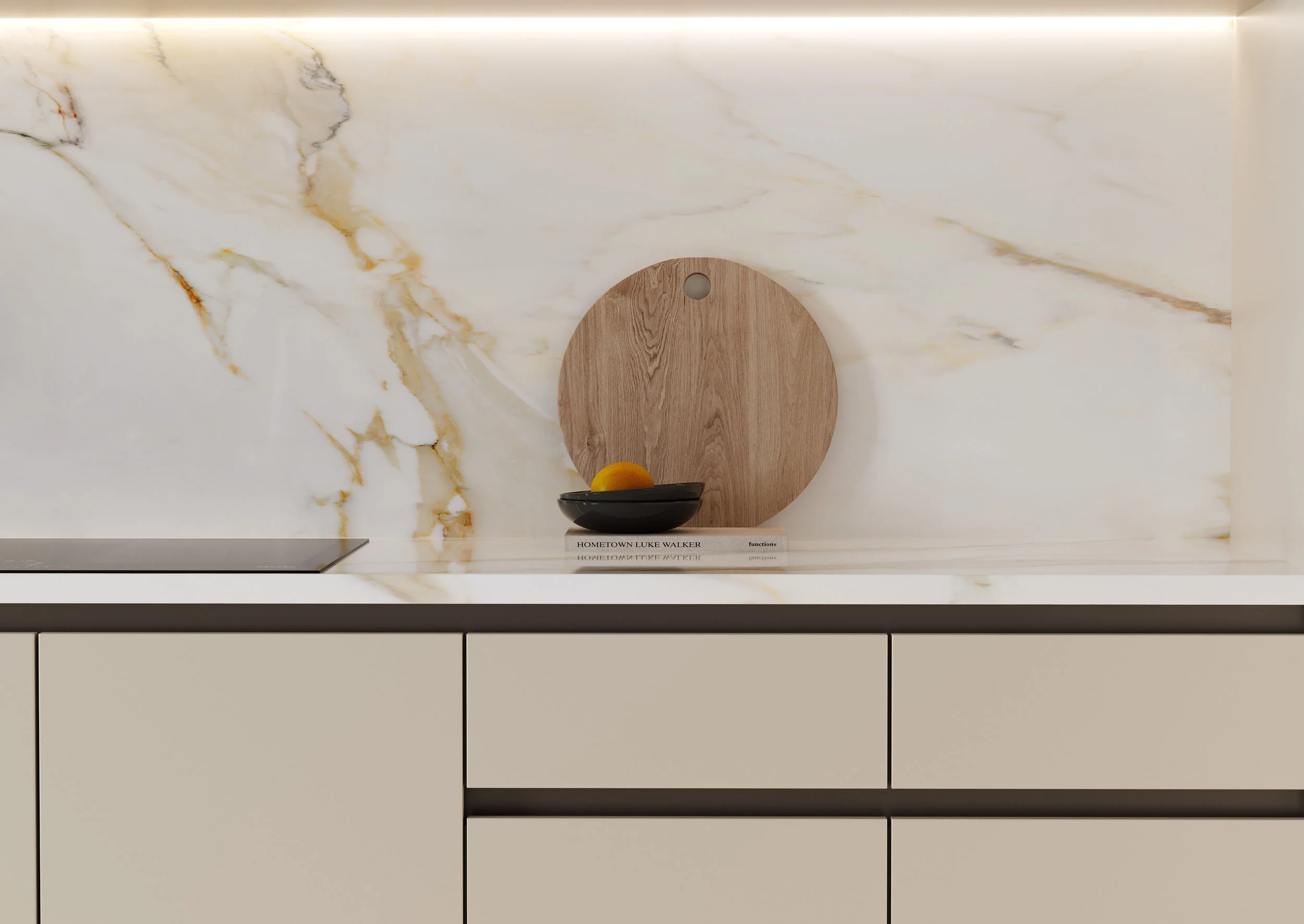 Minimalist kitchen countertop with a round wooden cutting board, a black bowl with a yellow fruit, and a book titled 'Hometown Luke Walker' against a white marble backsplash with gold veining.