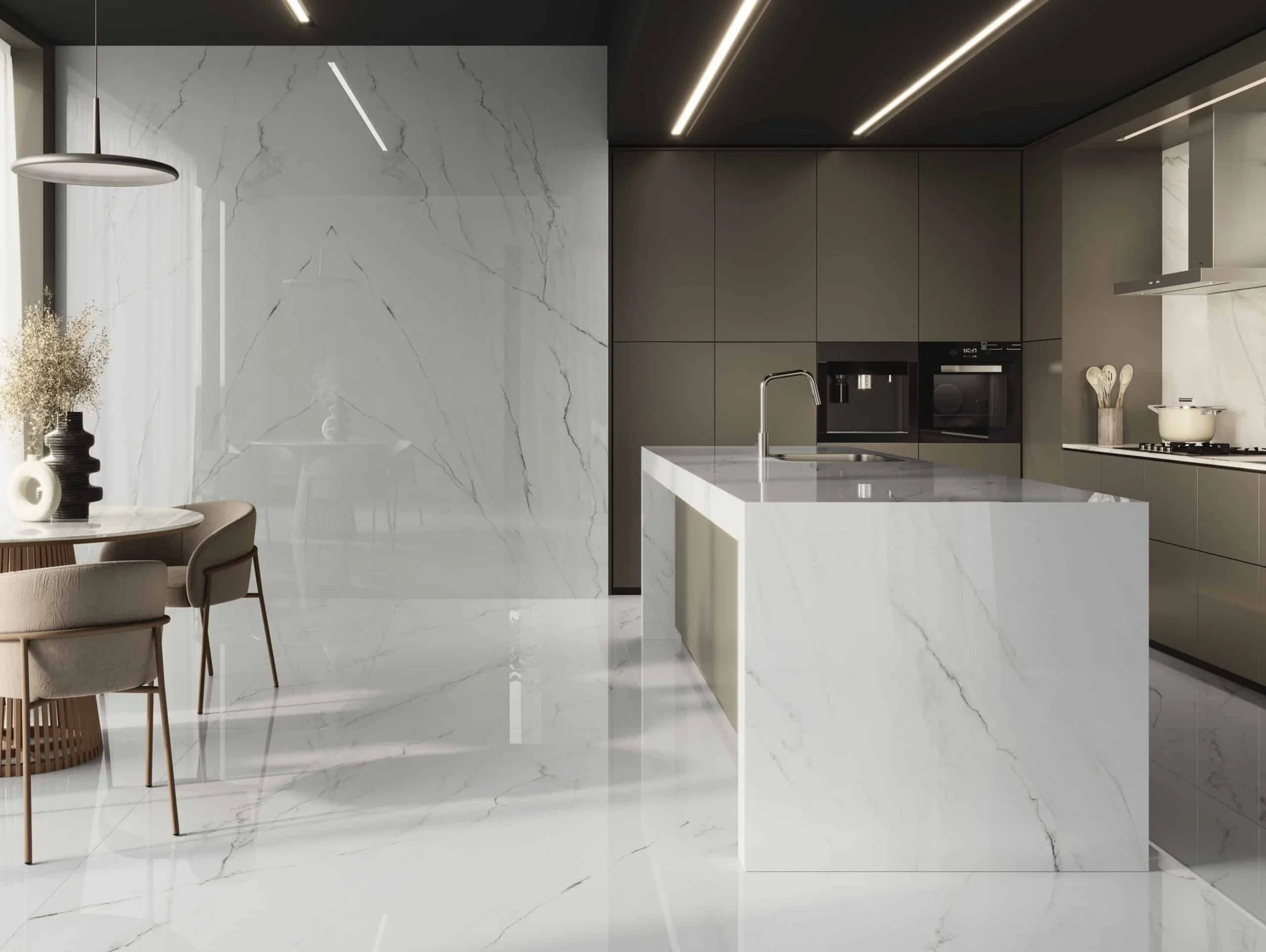 Modern kitchen with white marble island and floor, beige cabinets, black appliances, and a small dining area with beige chairs and a round table adorned with vases and dried flowers.