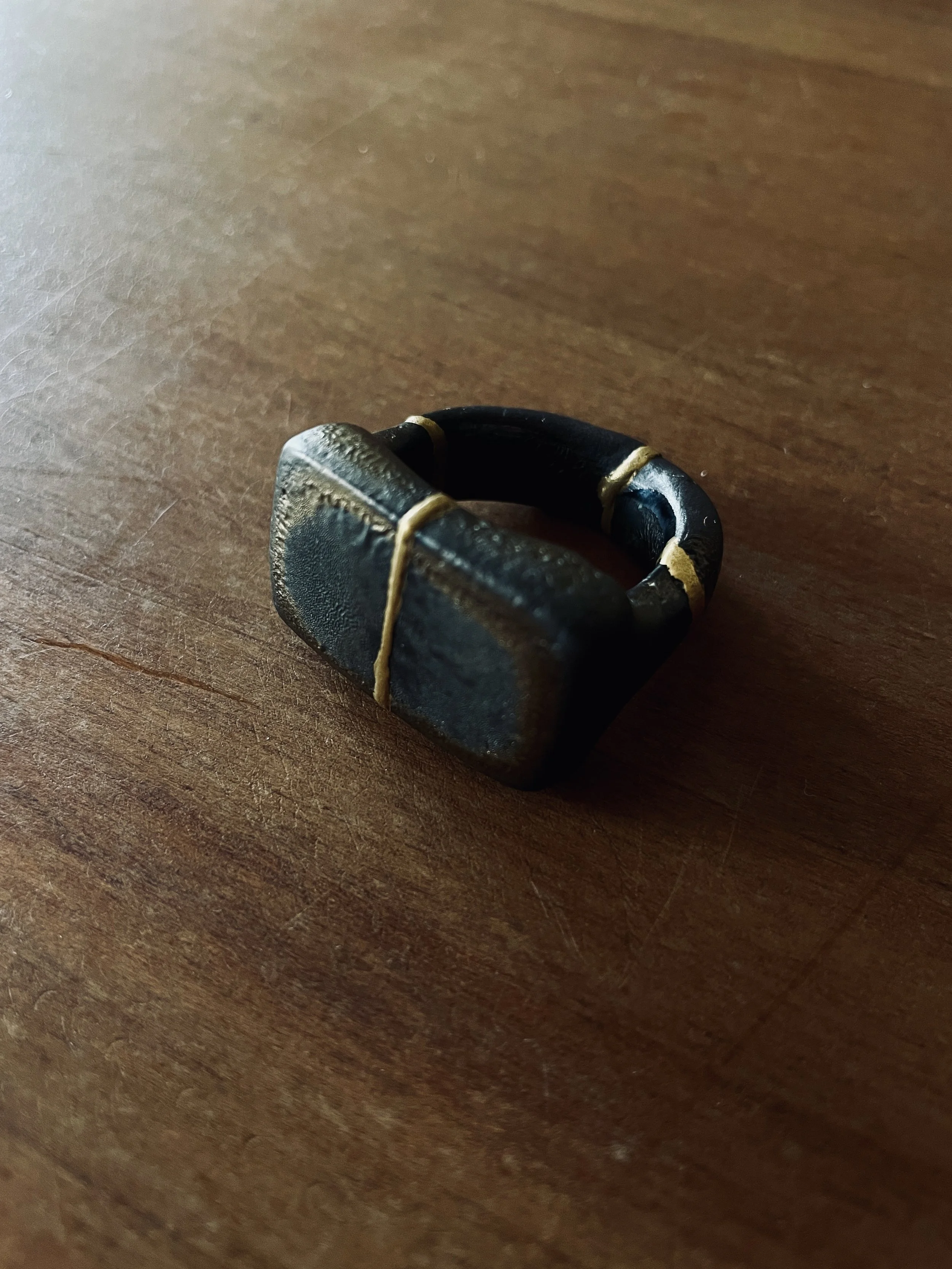 Une bague noire en forme de carré avec des accents dorés sur un fond en bois.