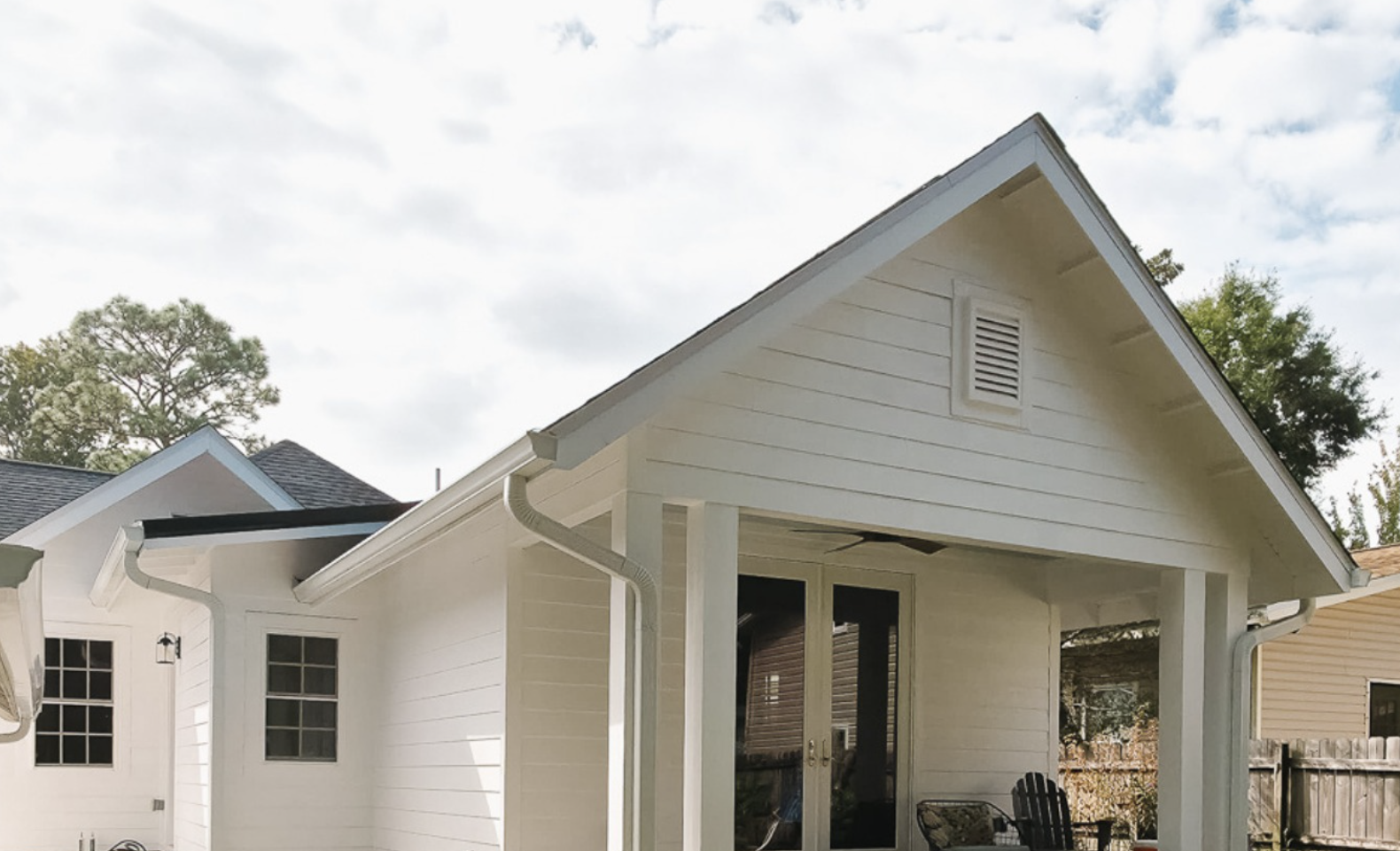 A white home addition with a clean gabled roof, updated shingles, and new gutters, shown from the backyard under soft winter light.