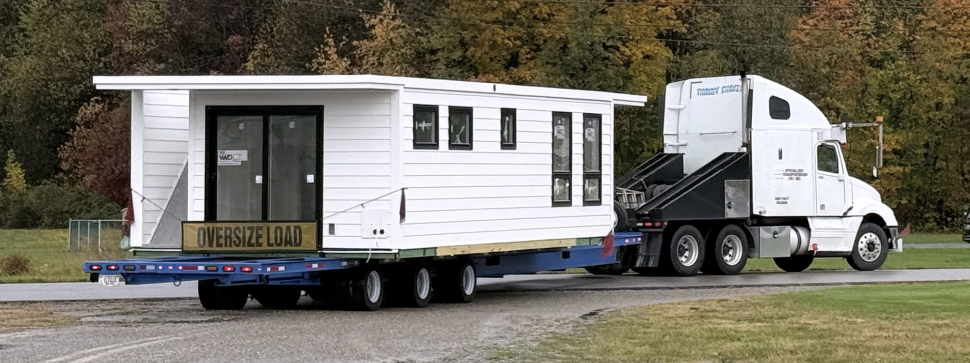 An image of a white houseboat on a semi truck in the fall
