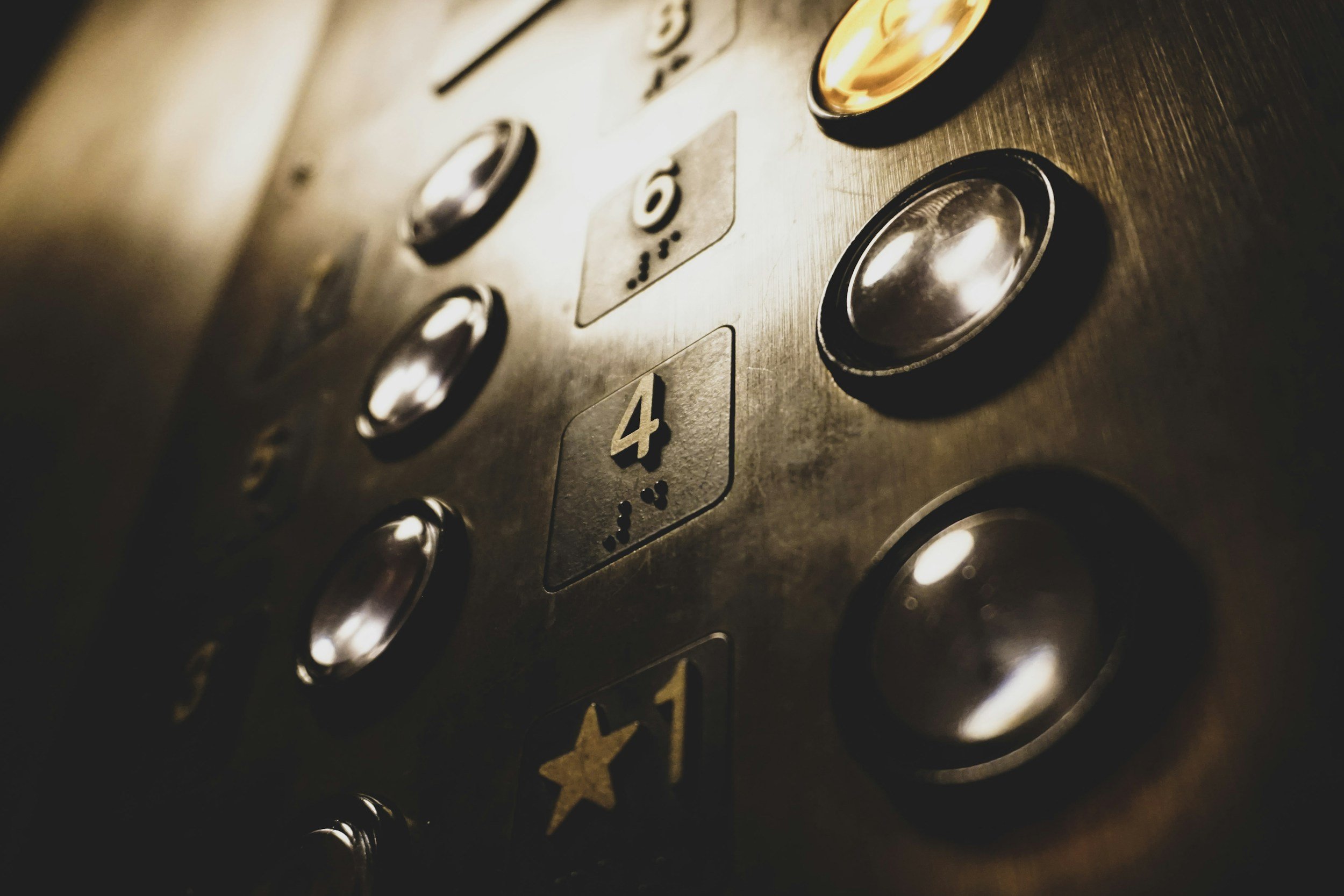 Close-up of elevator control panel with metallic buttons, showing buttons labeled with floor numbers 4 and 1, and various braille symbols.