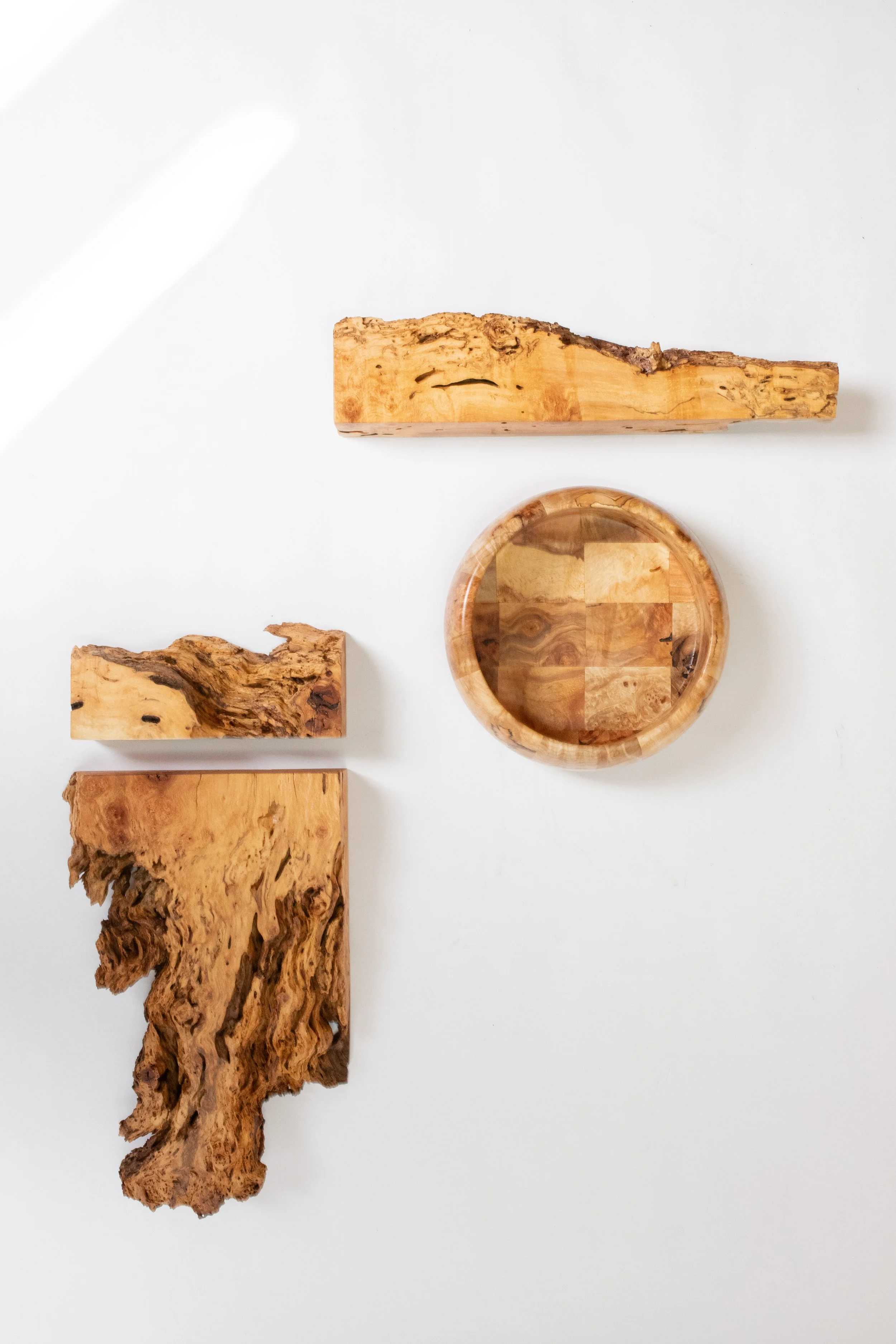 Three pieces of rustic wood, a small wooden bowl with a marbled pattern inside, all placed on a white surface