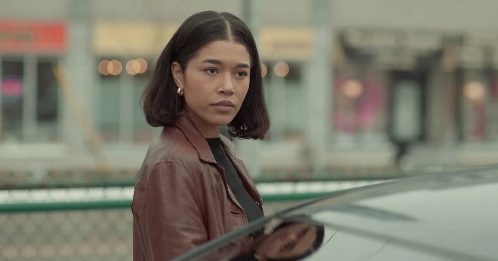 Savanah Bangoura standing outdoors beside a car in a film scene.