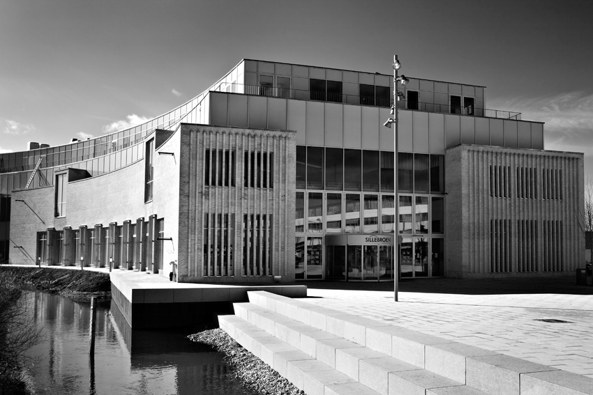 Sølvbroen, moderne bygning med store glasvinduer og betonfacade, ved vand med trin foran, i sort-hvid.