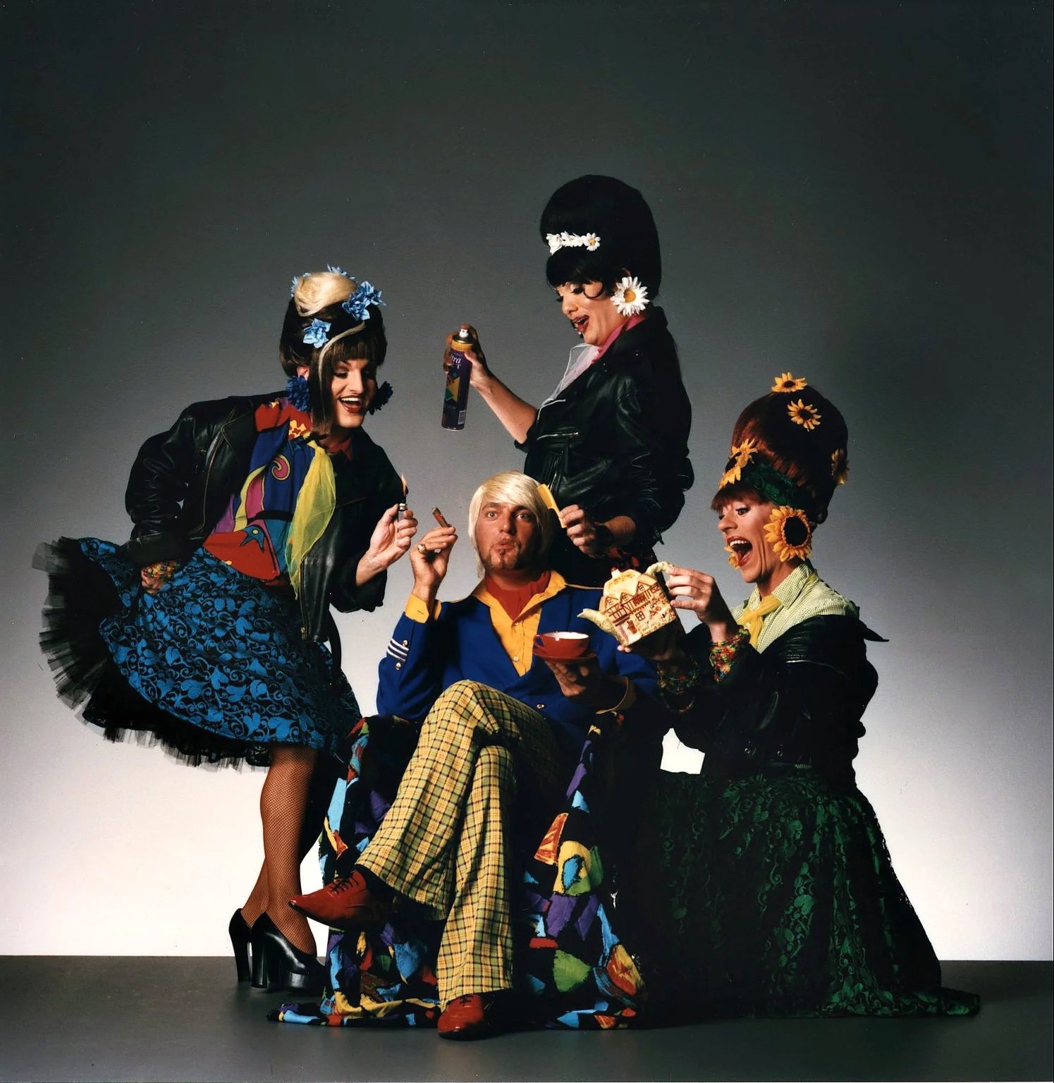 En gruppe fem personer iført farverige, 80'er inspirerede kostumer, der poserer med mad og drikke mod en enkel gradient baggrund.