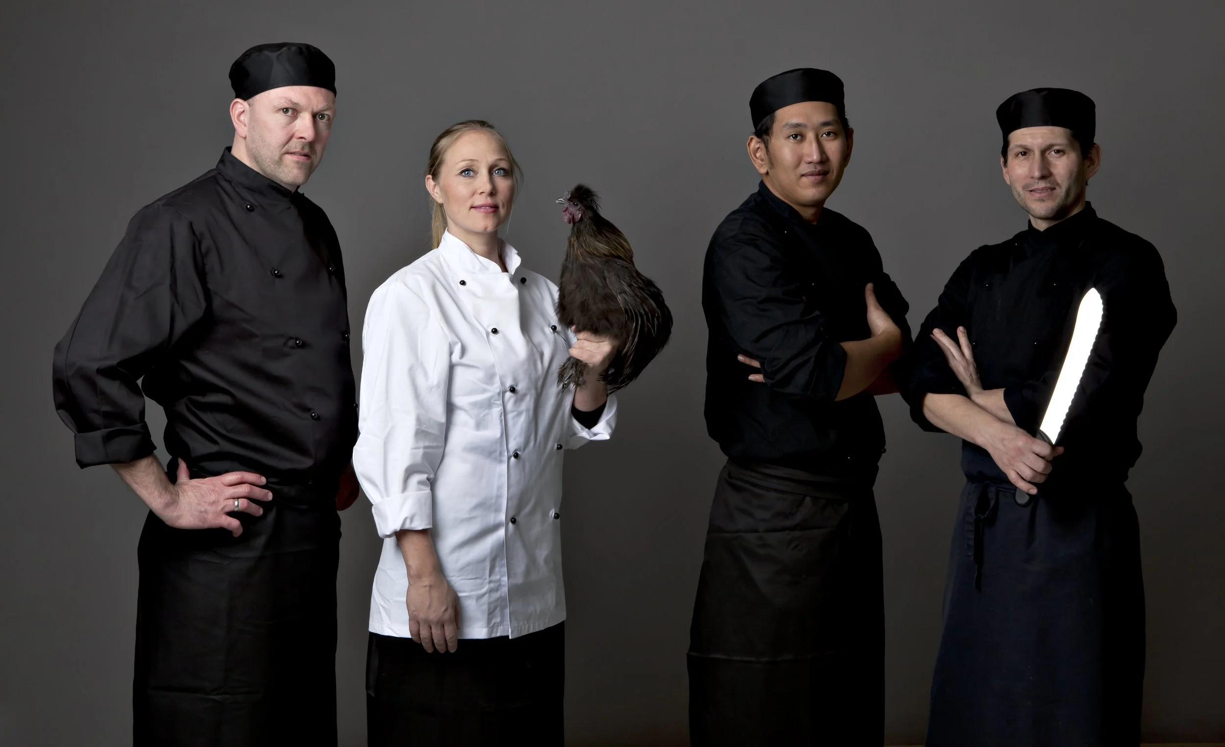 Fire manlige og en kvindelig kok, to af dem holder en høne, den ene mand holder en kniv med en lysende skærm.