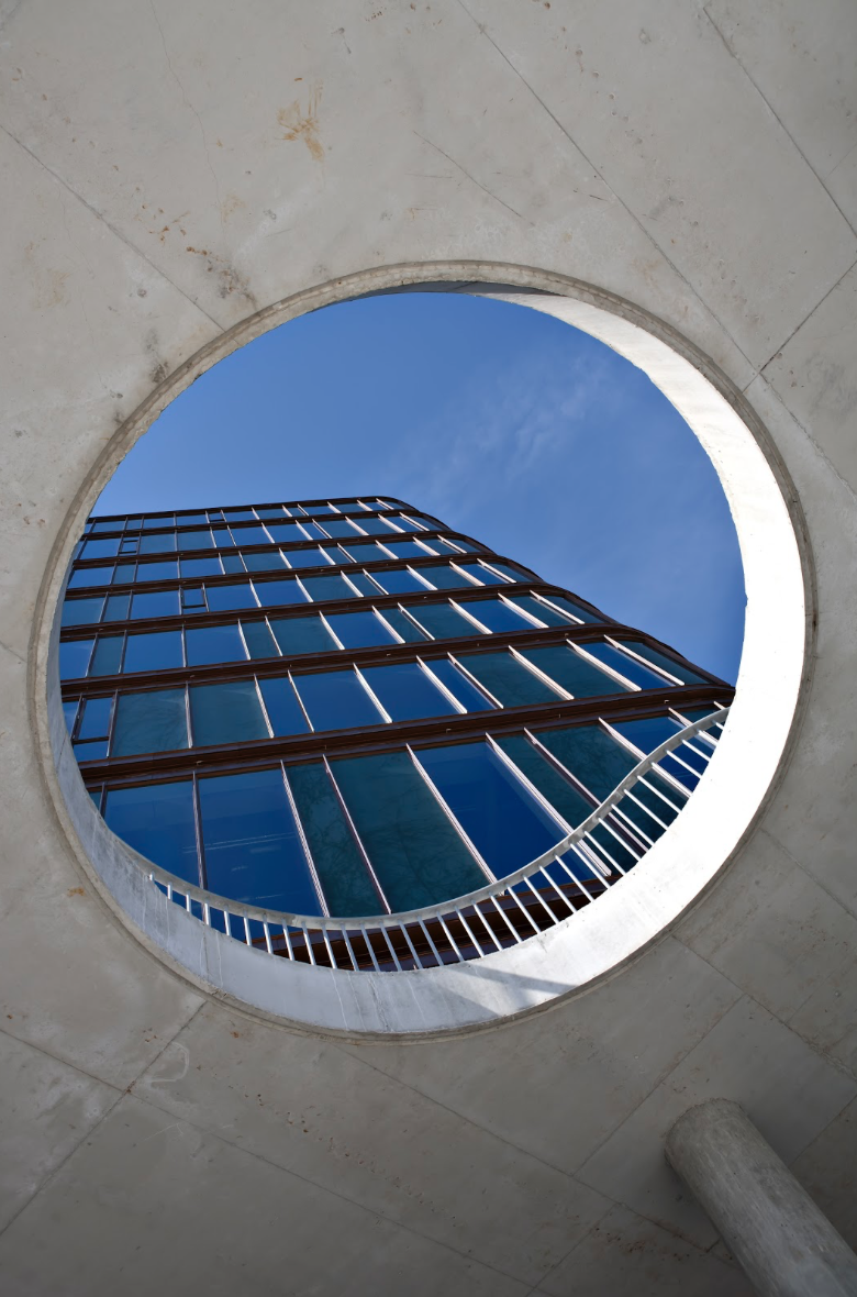 Udsigt op en moderne glasskyskraber set gennem et rundt åbning i en betonbygning
