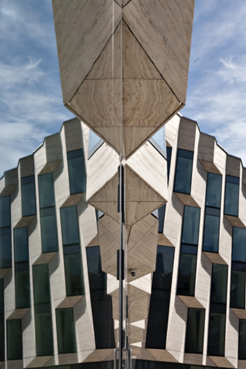 Fasade af modern bygning med geometriske vinduer, set fra jorden med en spejling af bygningen på jorden.