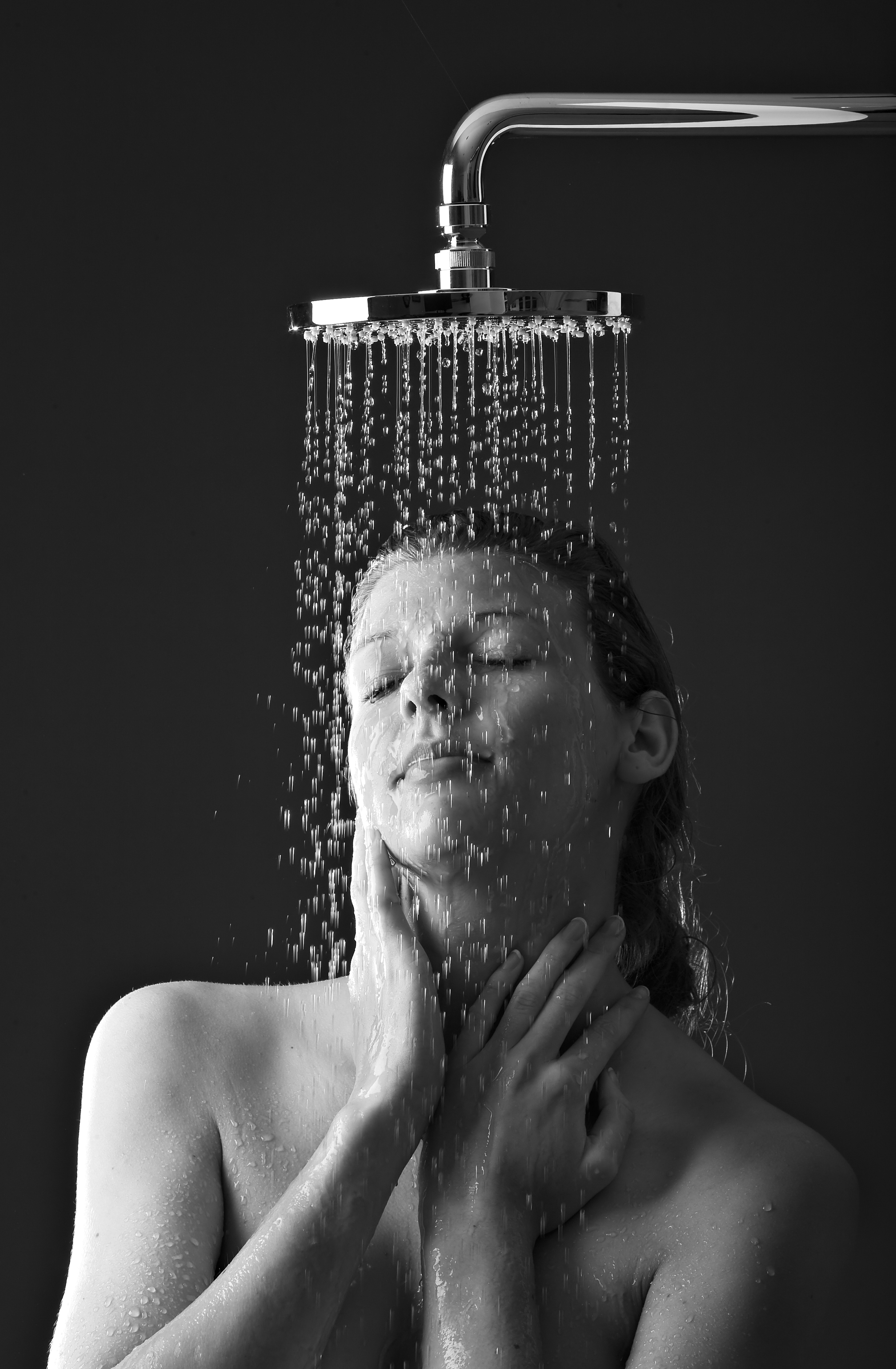 Sort-hvid foto af en kvinde under bruser, hun har lukkede øjne og hænderne eftersigende på halsen og nakken, mens vandet drypper ned over hende.