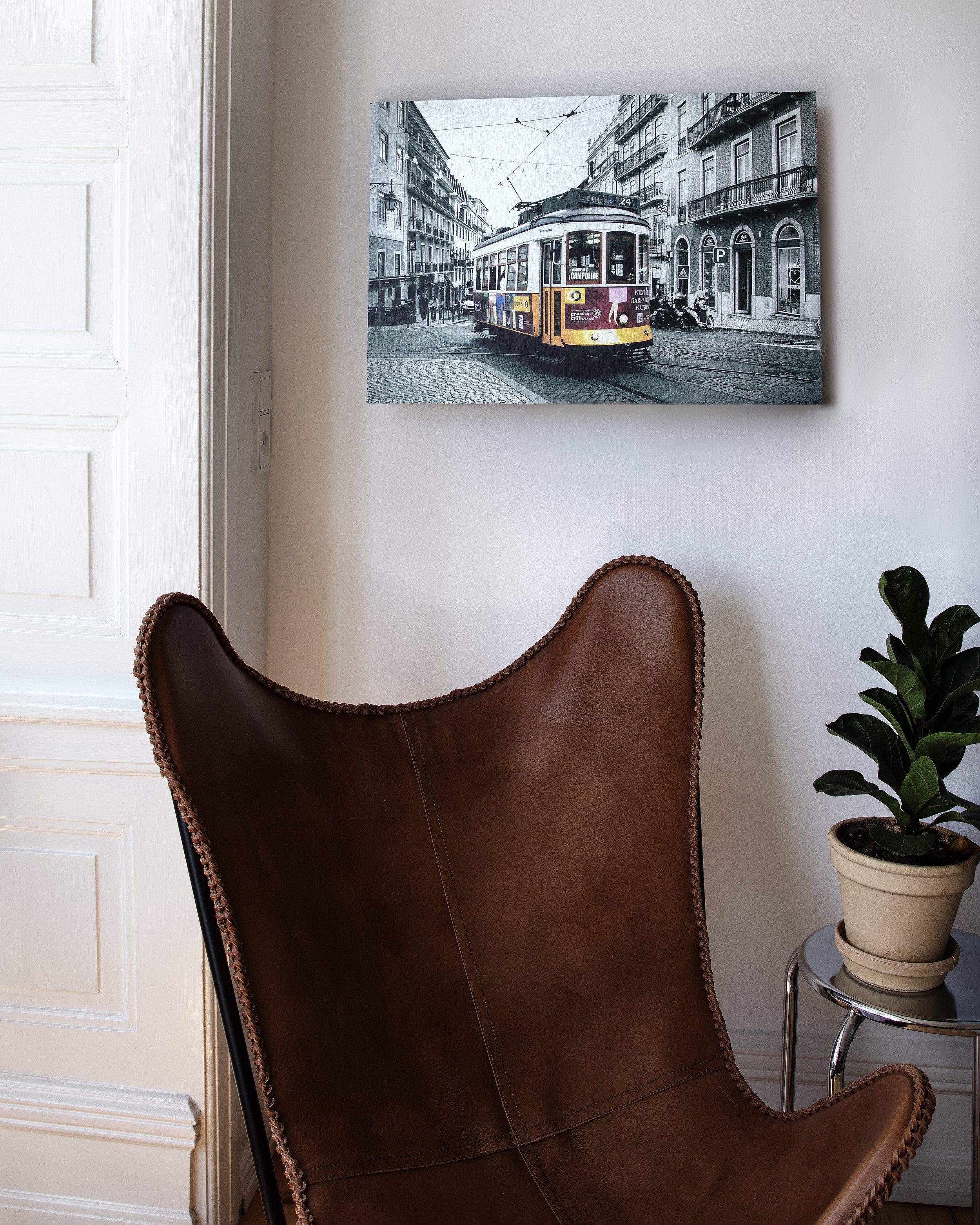 Fotografi af en vintage bytrikk på en stor sort og hvids foto med farvetrio i forgrunden, placeret på en hvid væg over en læderstol og en plante.