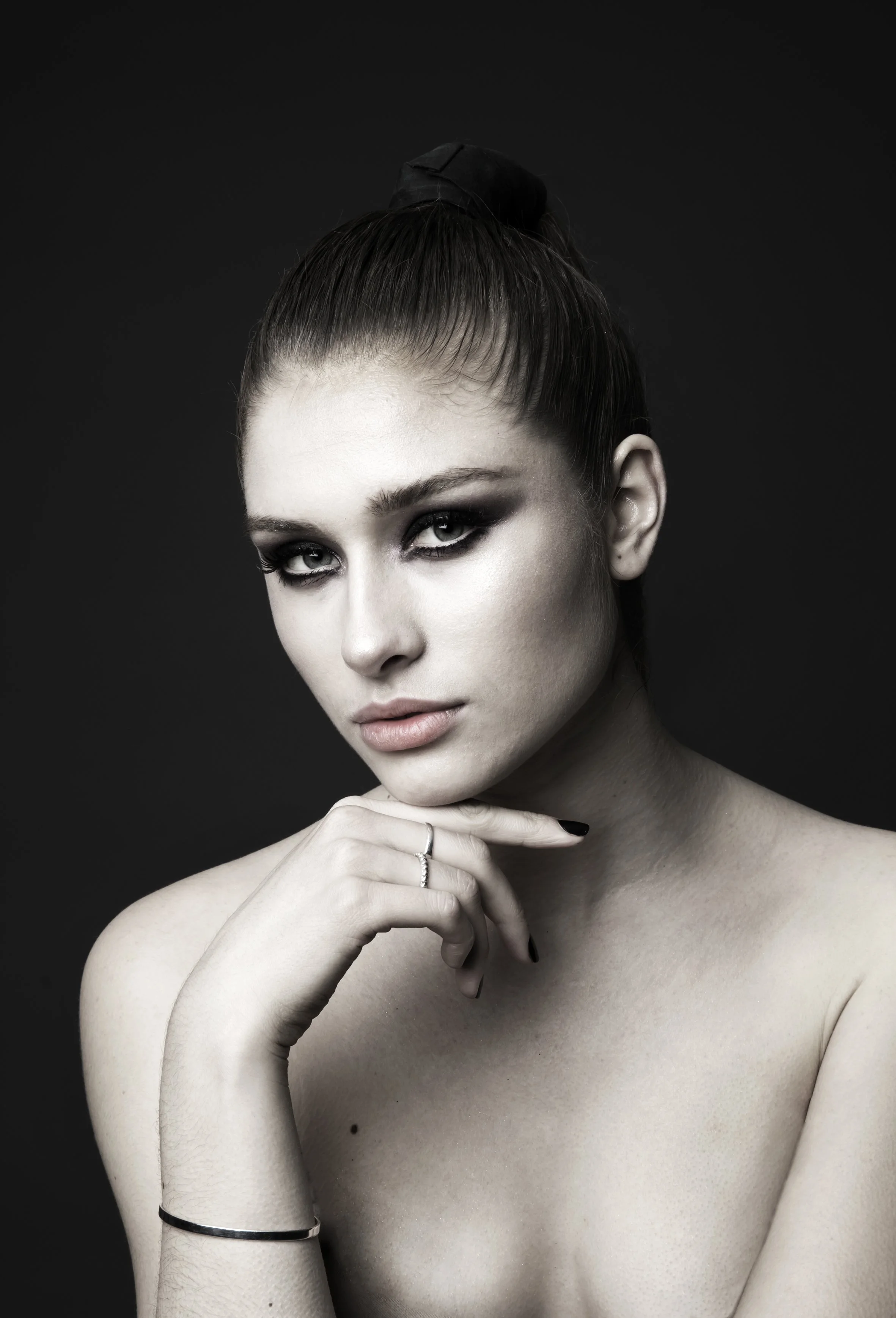 Sort-hvid portræt af en ung kvinde med stramt hår i en høj knude, let makeup, og en rolig, selvsikker udstråling, mod en sort baggrund.