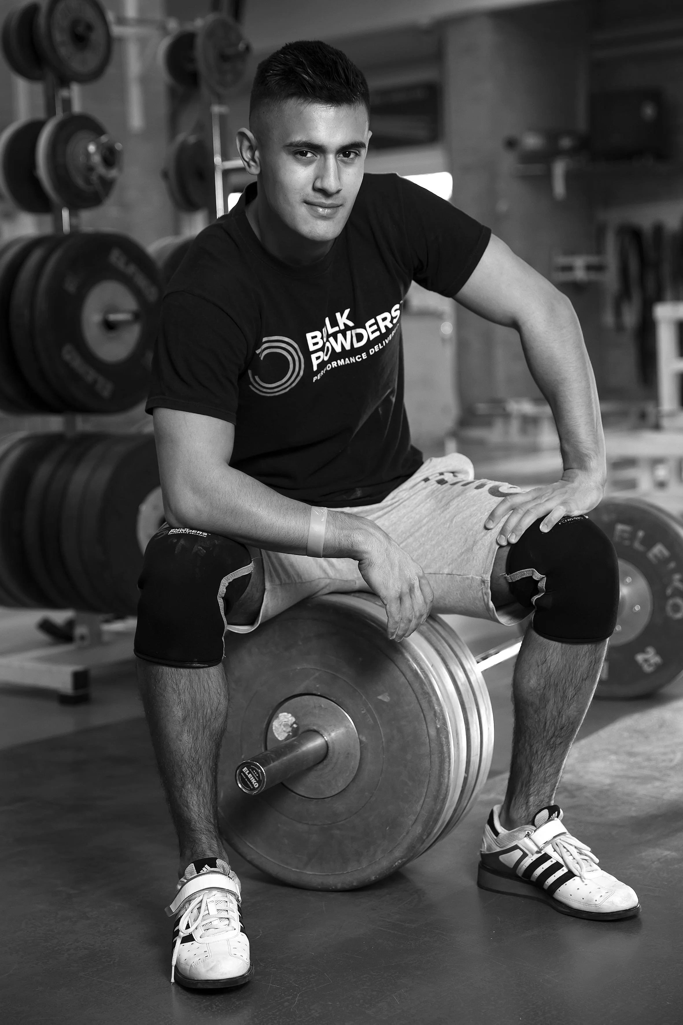 En mand sidder på en vægtstang i et fitnesscenter, omgivet af vægte.