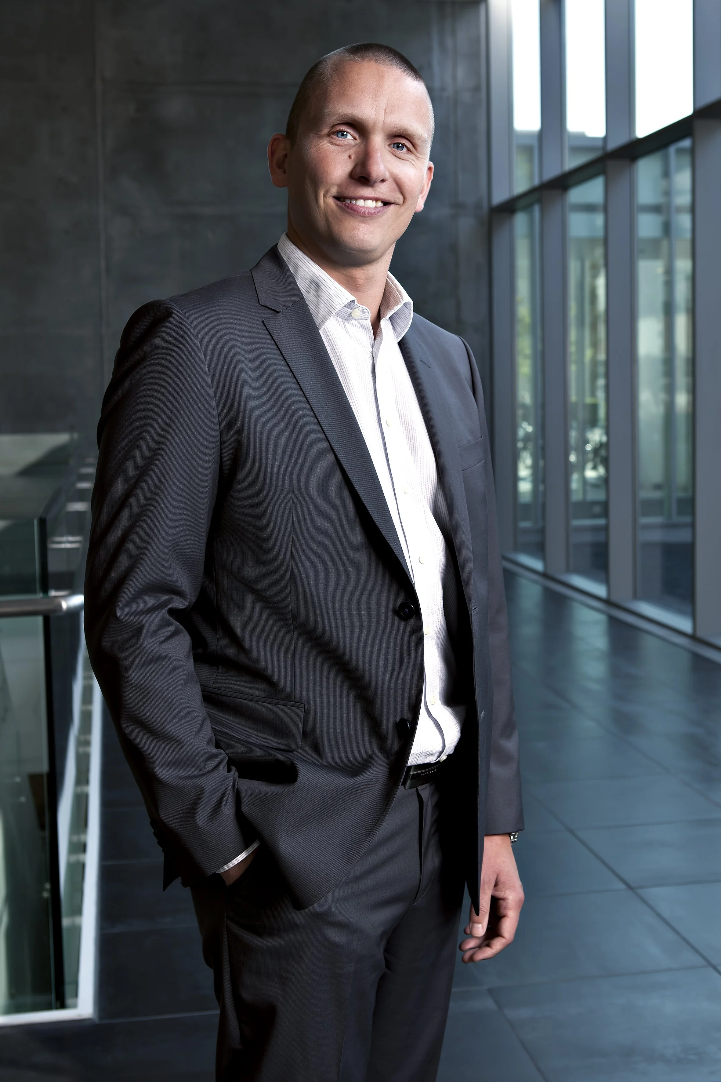 En mand i businessdragt står i en moderne kontorbygning med store vinduer og naturligt lys.