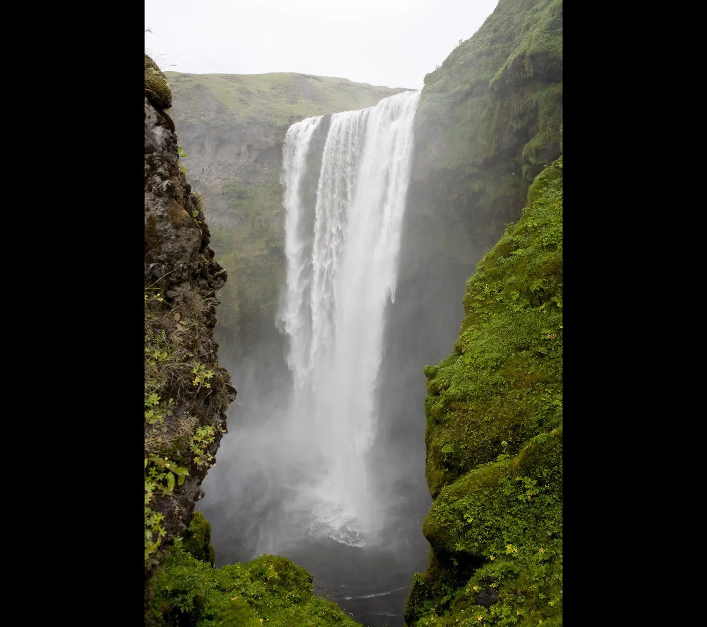 Fosfaldet waterfall i Island omgivet af grønne mosbeklædte klipper.