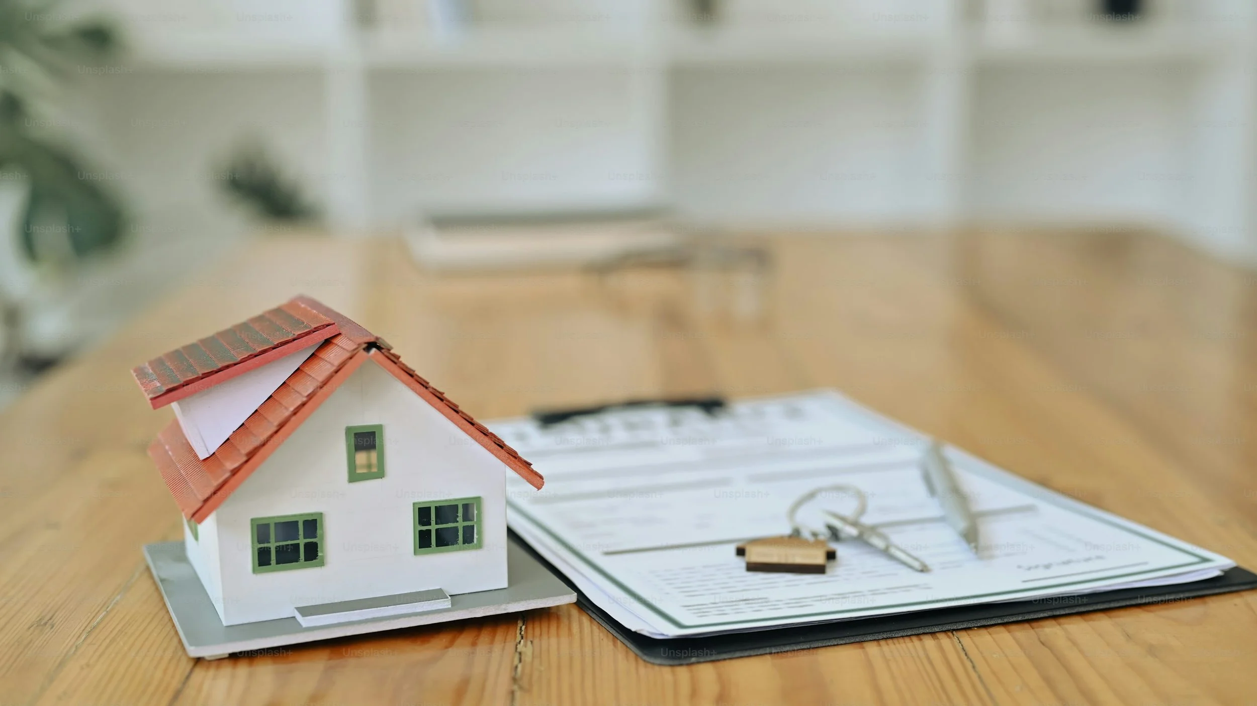 Model house, keys, and a pen on a clipboard on a wooden table, representing real estate or home sale.