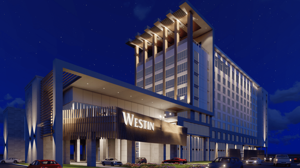 Nighttime exterior view of a modern hotel building with the sign 'Westin' on the front, illuminated with architectural lighting, cars parked in front, and a starry sky in the background.