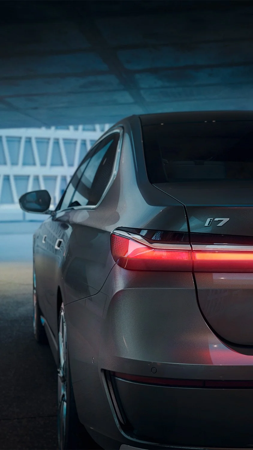 Rear view of a gray electric car parked under a bridge, with a modern architectural building in the background, nighttime city scene.