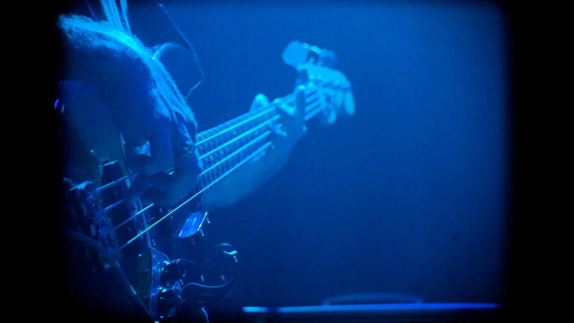 Close-up of a guitar being played, with the musician's hand on the fretboard, scene illuminated in blue light