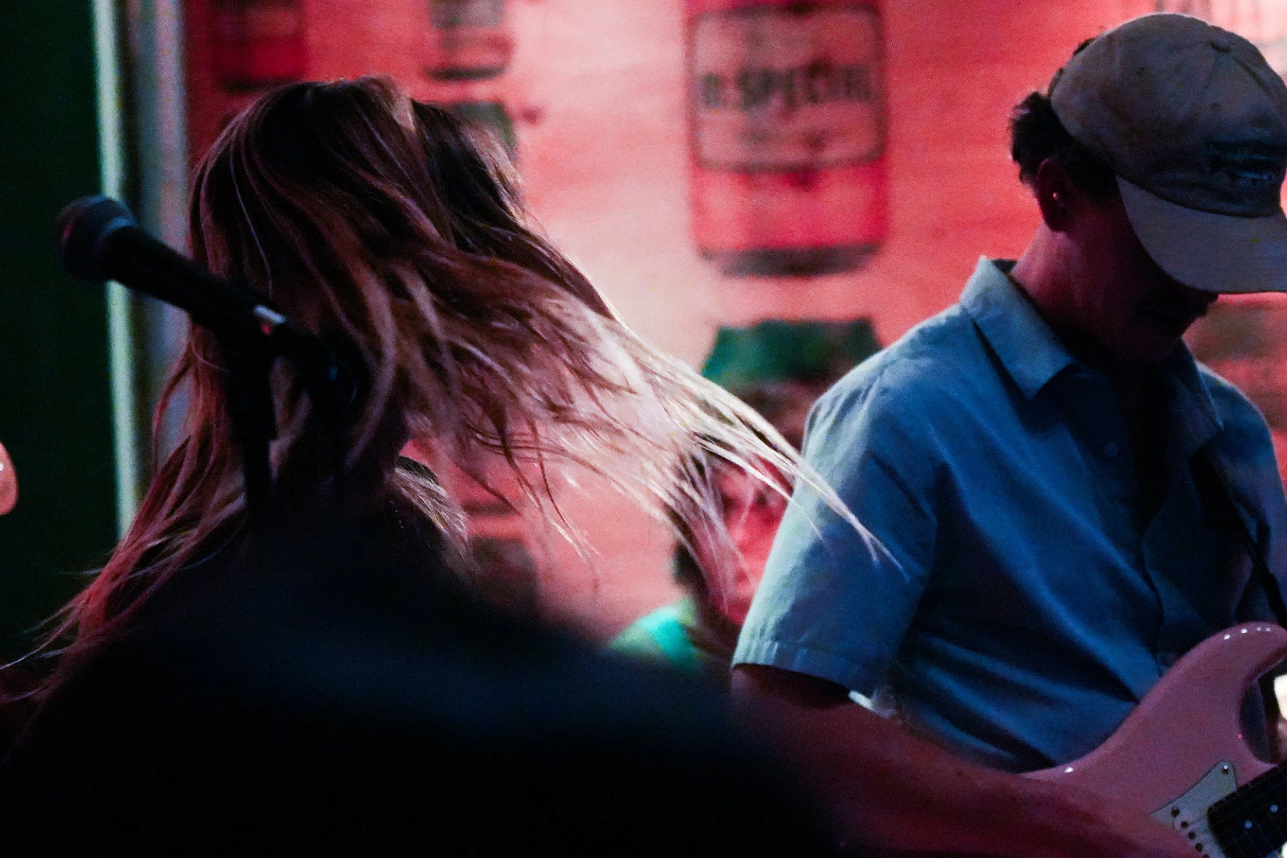 A woman with long hair and a man wearing a cap and sunglasses playing a guitar on stage.