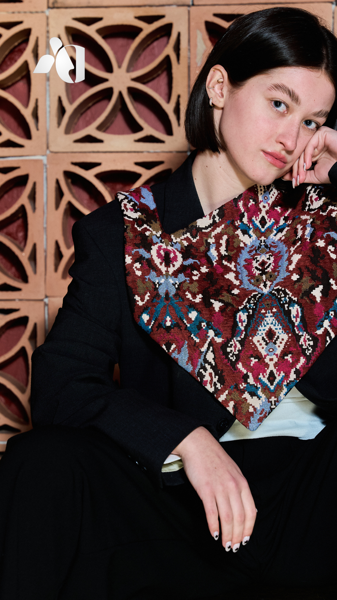 Jeune femme aux cheveux noirs, portant un patchwork orange, entourée de briques décoratives.