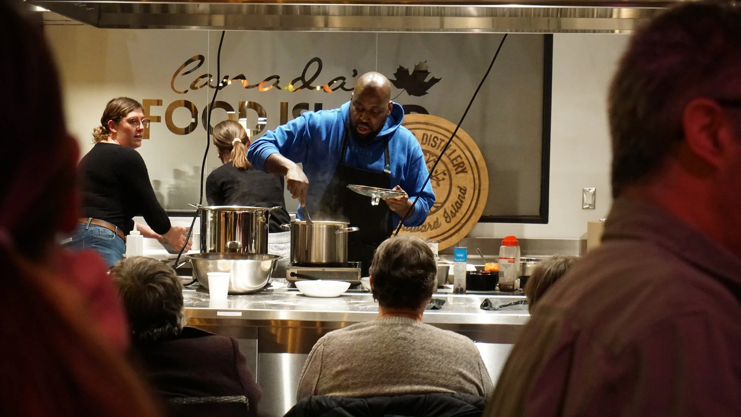Chef cooking on stage at Canada's Food Mixer event, with audience watching.