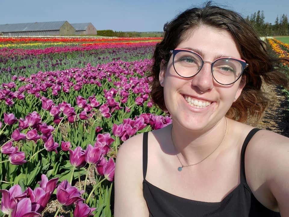 A woman with short brown hair and glasses taking a selfie in a field of colorful tulips.