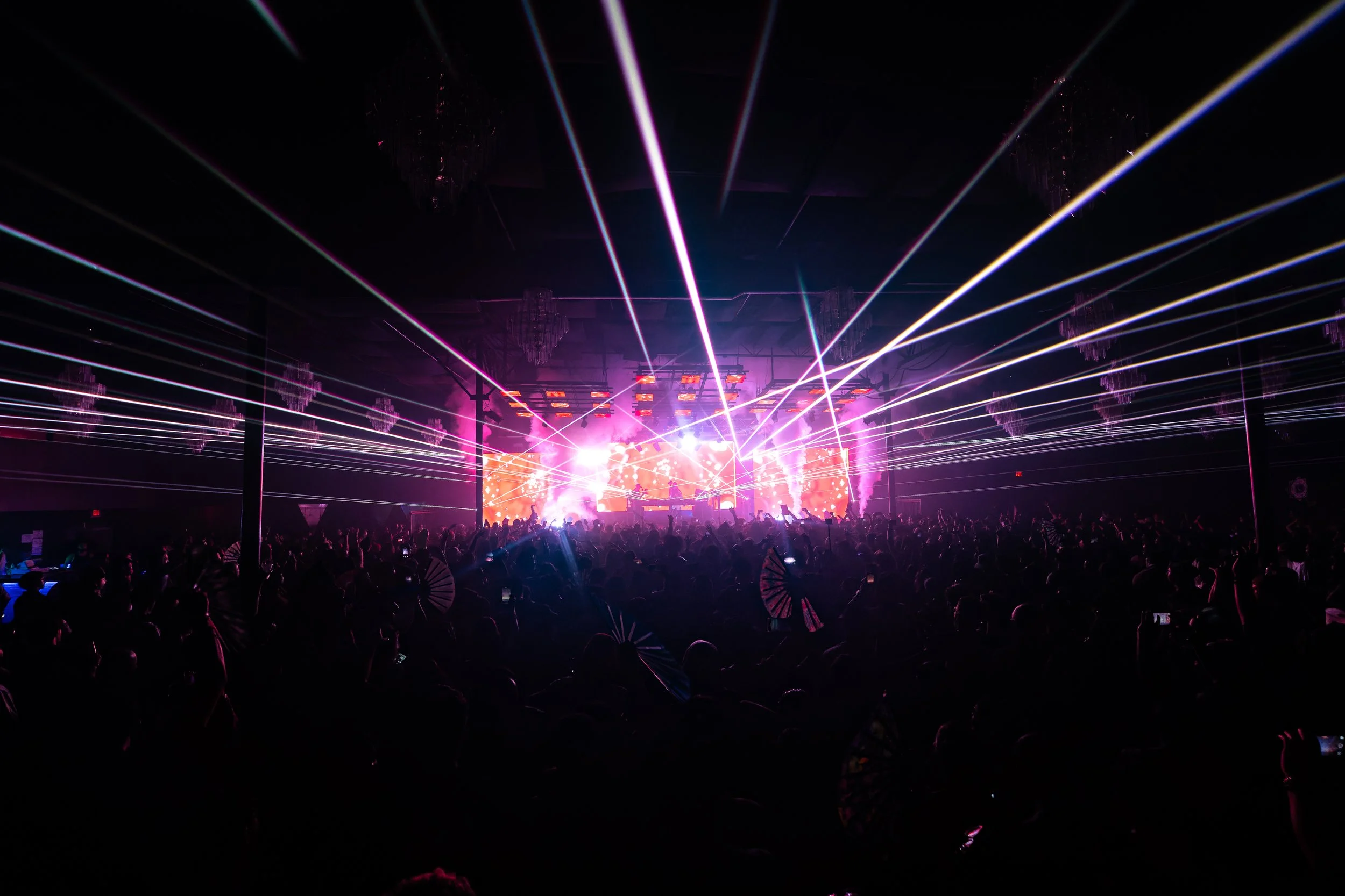 A concert or music festival with a large crowd and colorful laser lights on stage.