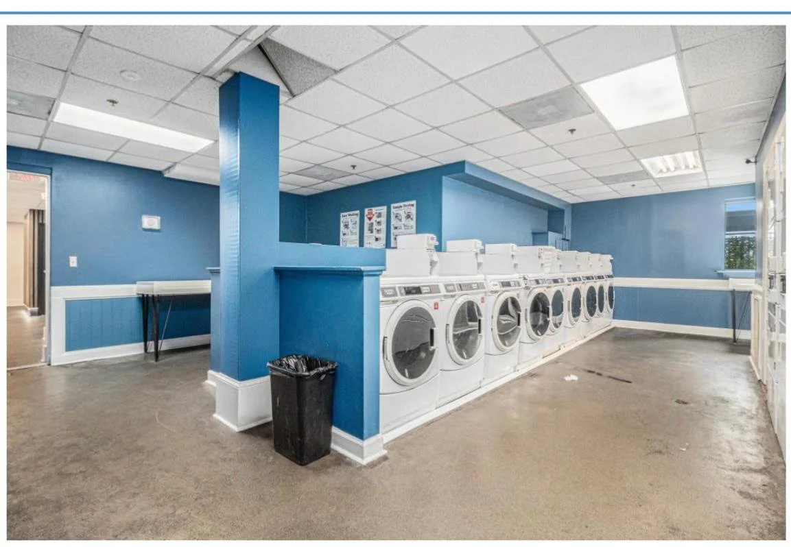 Row of industrial washing machines in a laundry room with blue walls and a beige floor.