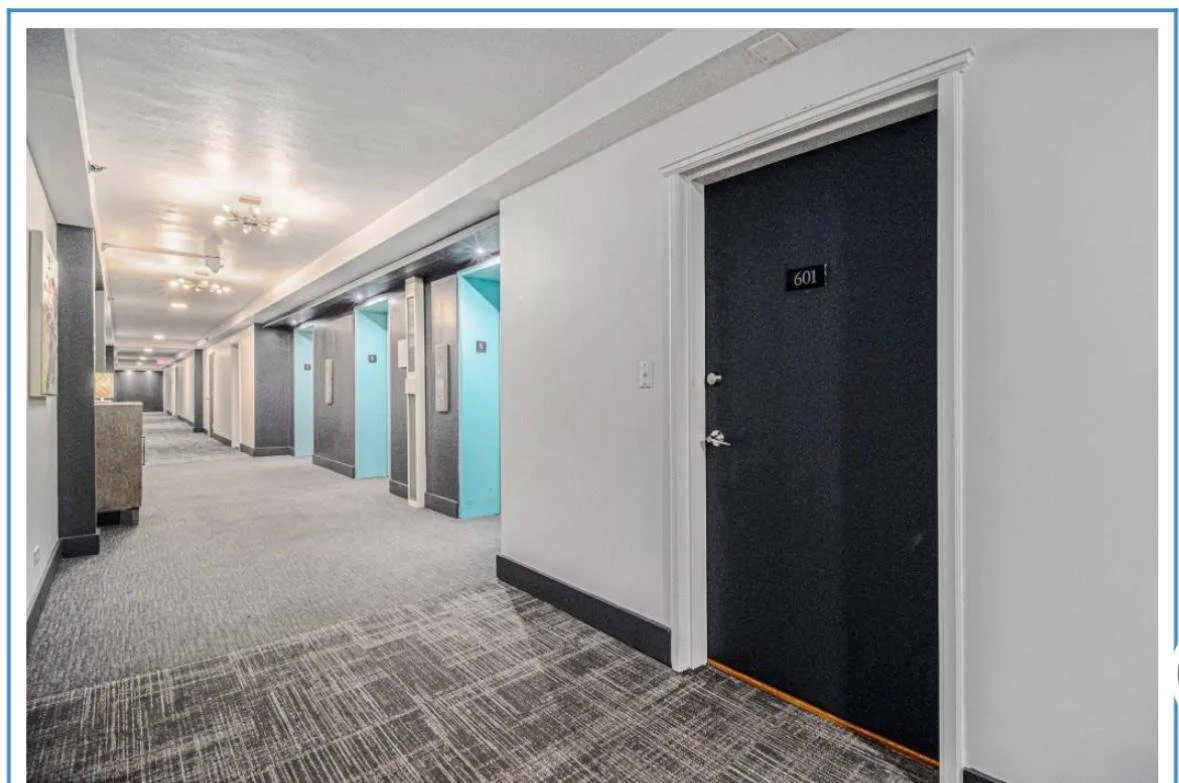 Interior view of a hotel corridor with multiple elevators, a black door labeled 601 on the right, and ceiling lights.