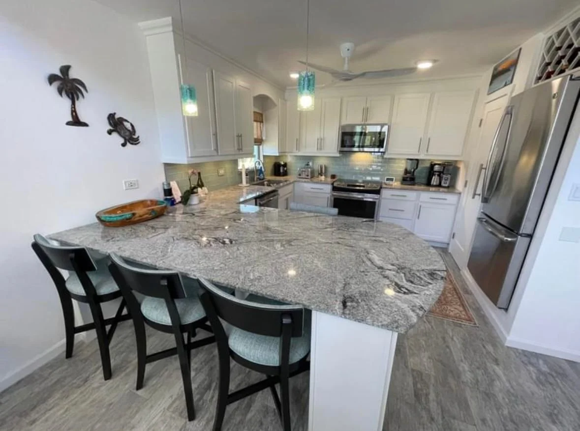 Modern kitchen with white cabinets, granite island, stainless steel appliances, and coastal decor