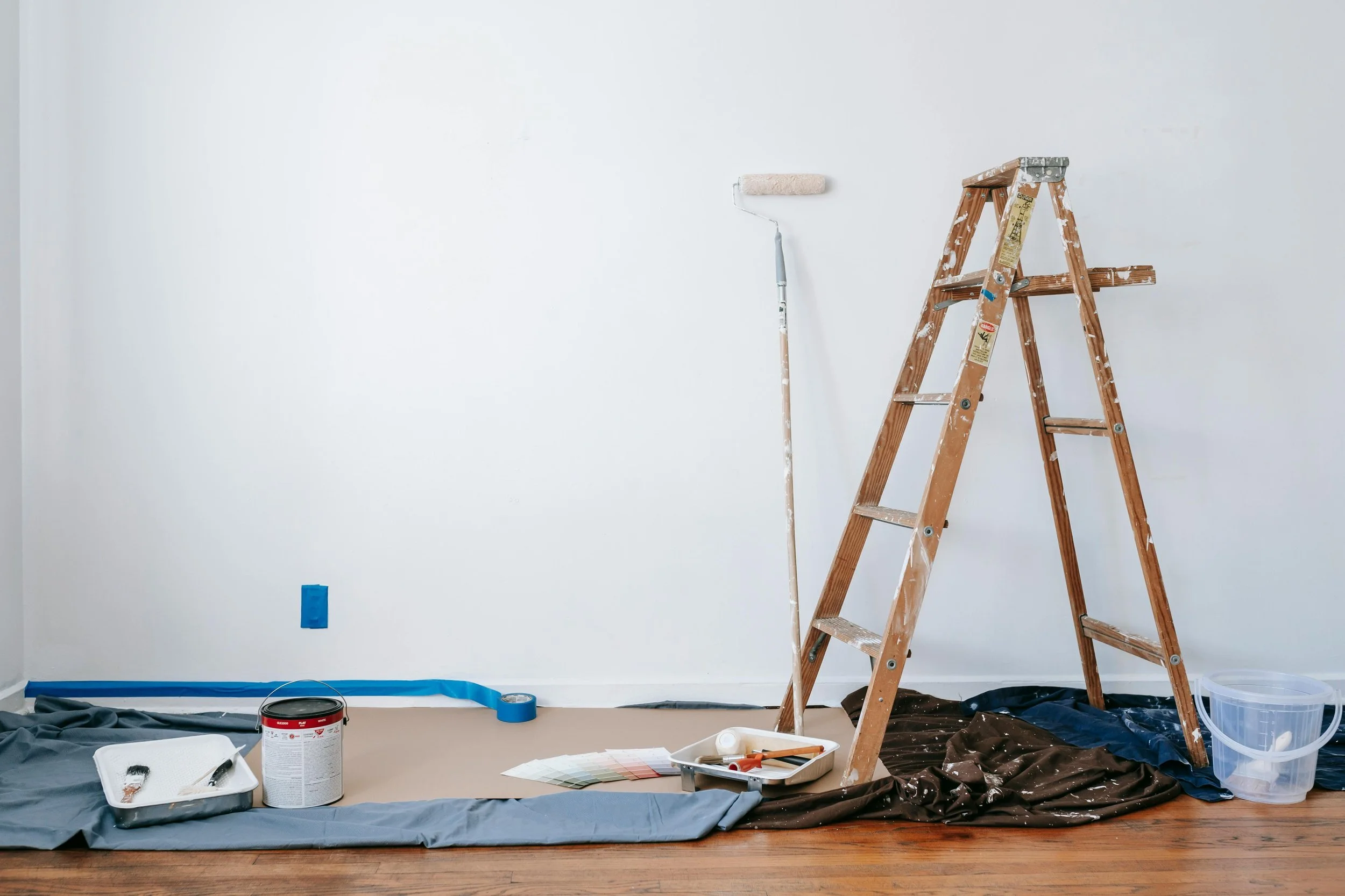 A painting scene: white walls, a wooden ladder, paint supplies, and a roller. GLO assists with Lead based paint disclosures. Contact Geraghty Law Office: Real Estate & Business Law. Trusted Legal Support in Denver, Colorado.